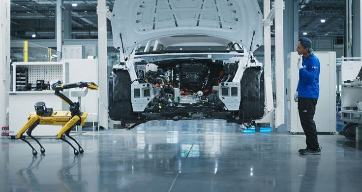 The SPOT robotic dog is standing in a production hall with a man.